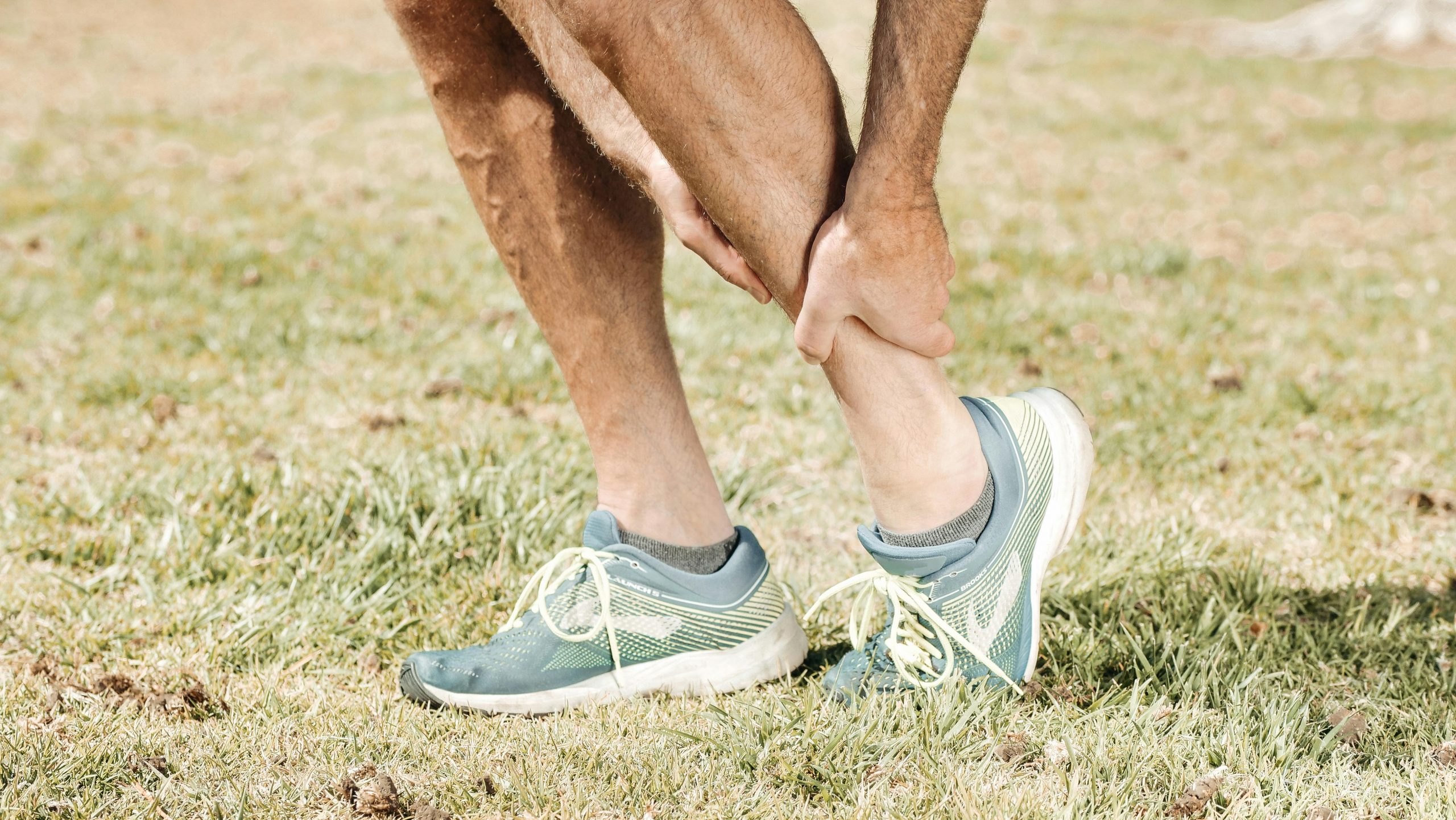 man in athletic shoes clutching his ankle