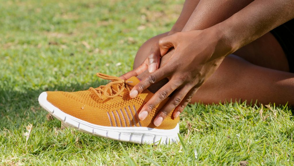 athlete wearing yellow running shoes holding their ankle, appearing to be in pain